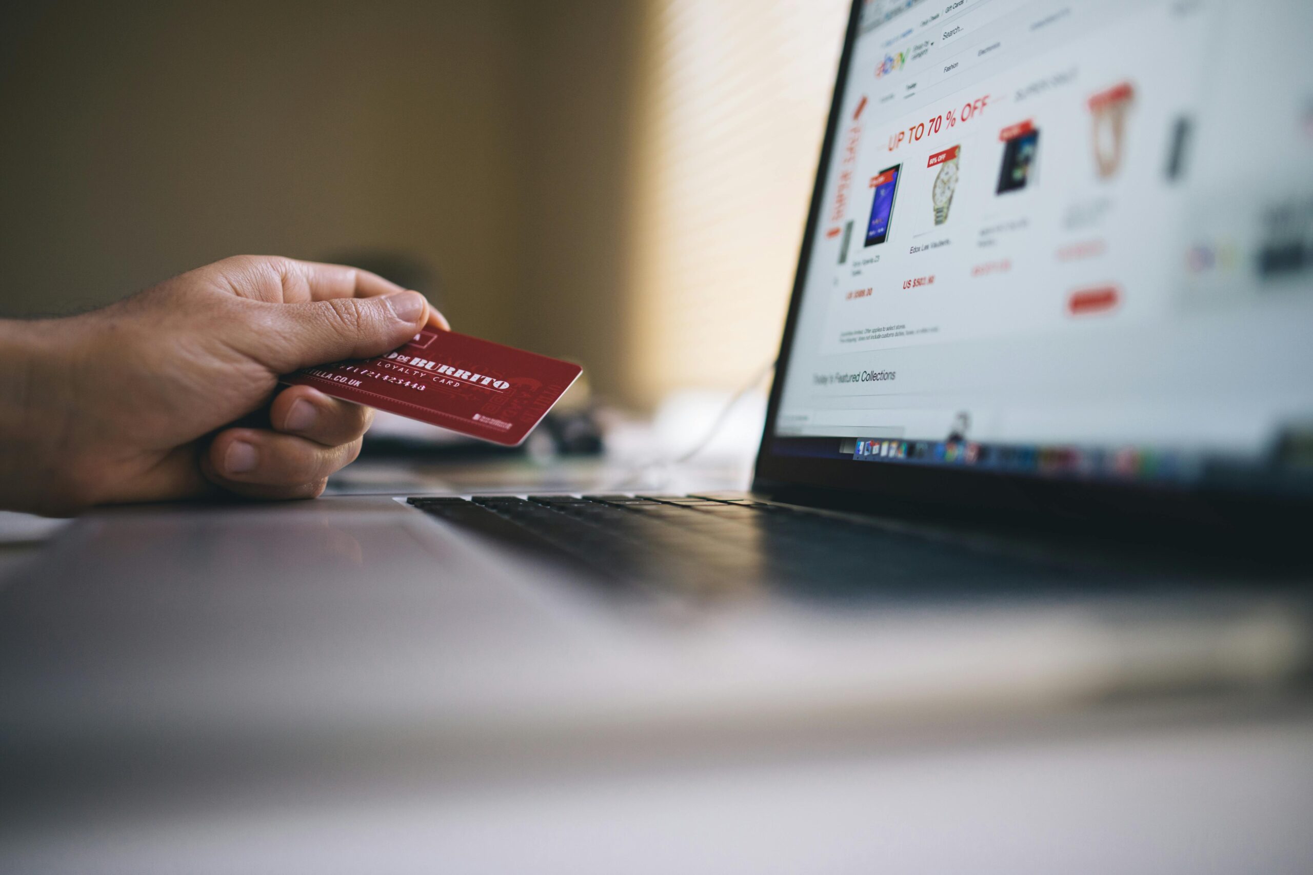 Usługi Person holding a credit card while shopping online on a laptop, indicating ecommerce transactions.